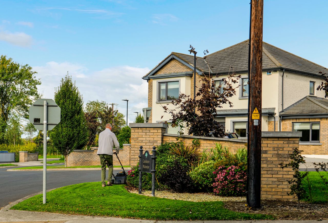 our-story A man mowing the lawn outside a modern suburban home with a lush garden and clear blue sky.