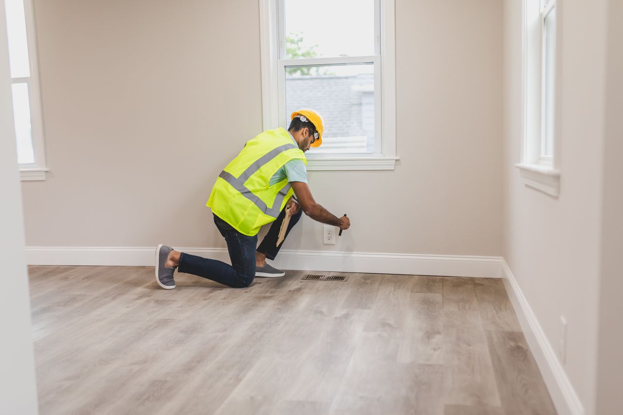 why-choose-us A home inspector in high visibility vest examines an electrical outlet in a modern room.